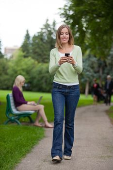 Full length of a young woman reading text message as she walks in park