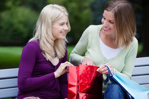 Happy smiling woman sitting on park bench looknig at purchases