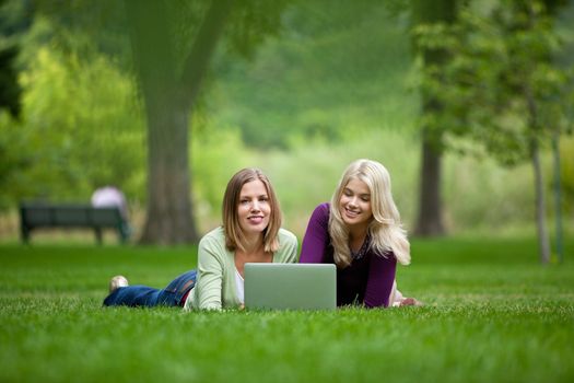 Happy young women with laptop lying on grass