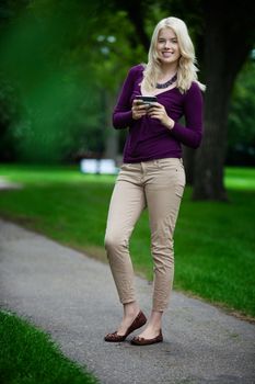 Portrait of attractive young smiling woman using cell phone in park