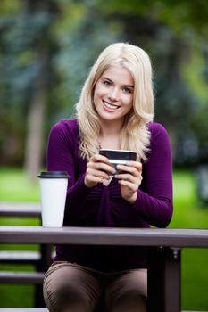 Portrait of happy smiling young woman with cell phone in park