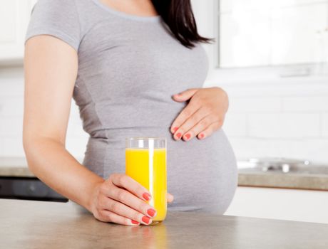 Woman in third trimester holding orange juice in kitchen
