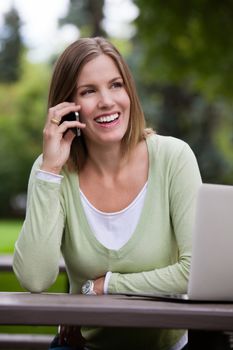 Portrait of happy young adult talking on cell phone in park