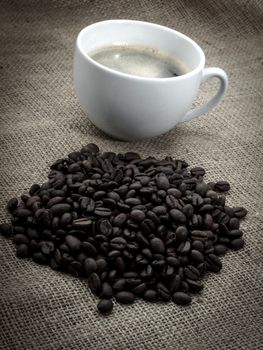 Black coffee bean with coffee cup, over old burlap background