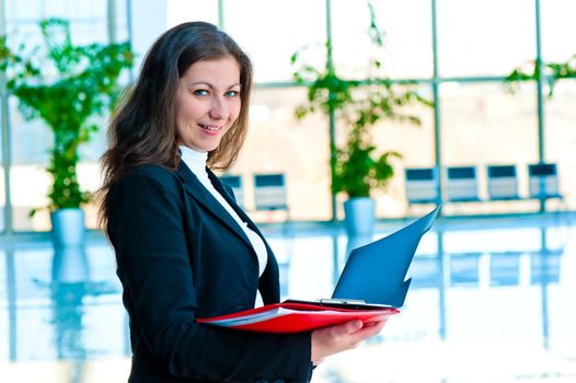 Happy businesswoman holding an open folders on the background of office interior