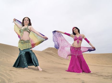 Portrait of two arabic dancers at desert holding clothes while dancing