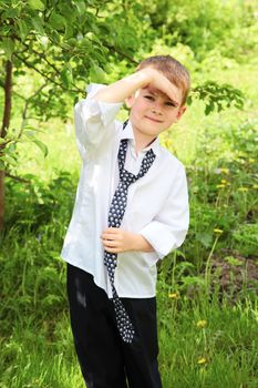 The little boy unties a tie against green leaves