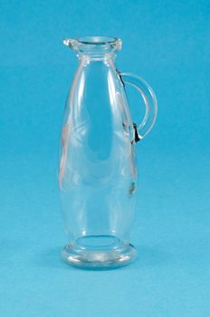 old transparent empty glass jug jar with handle on blue background.