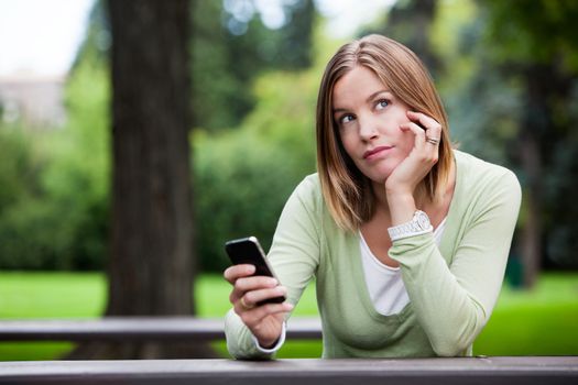 Thoughtful woman in park with smart phone