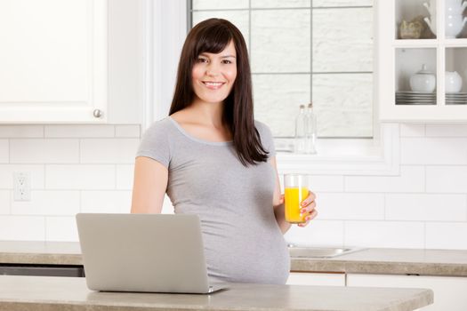Happy pregnant woman in kitchen using laptop computer