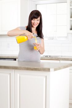 Happy pregnant mother pouring orange juice in kitchen