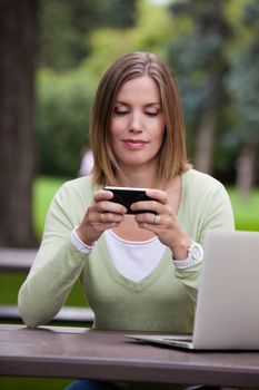 Woman creating a status update with mobile phone in park