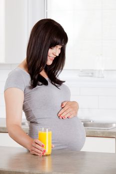 Pregnant happy mother with glass of orange juice looking down at belly