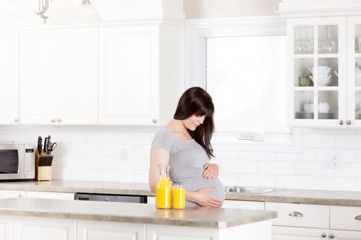 Pregnant woman at home in kitchen with orange juice