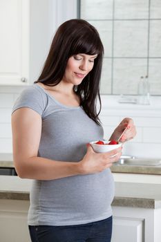 Pregnant woman eating healthy bowl of fruit in kitchen