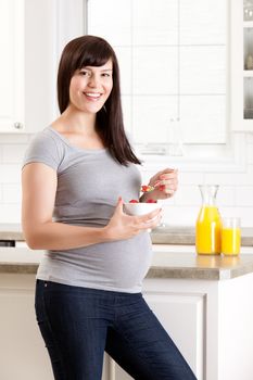 Happy pregnant woman in third trimester eating breakfast in kitchen