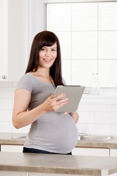 Portrait of a pregnant woman holding a digital tablet at home in kitchen
