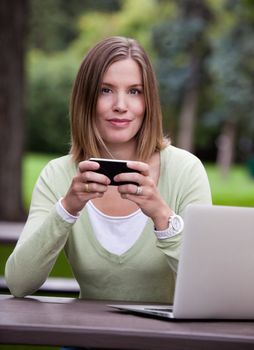 Portrait of attractive woman in park with mobile phone and computer