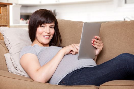 Happy smiling pregnant woman on sofa with digital tablet