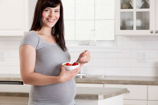 Smiling healthy pregnant woman with breakfast of granola and strawberries.