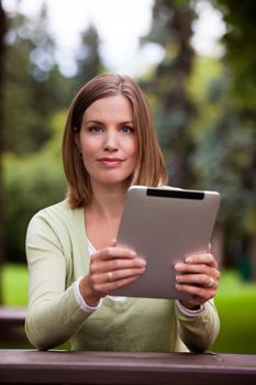 Portrait of attractive young woman in park holding digital tablet