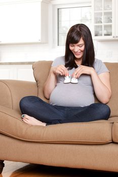 Portrait of a happy young pregnant woman holding baby shoes on belly