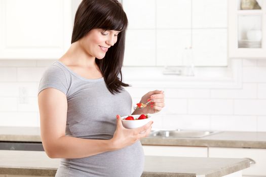 Happy healthy pregnant woman in kitchen eating healthy snack