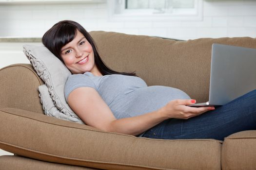 Portrait of pregnant woman using laptop while lying on sofa