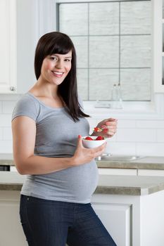 Portrait of pregnant woman eating healthy bowl of fruit in kitchen