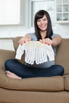 Portrait of happy pregnant woman holding baby clothing while sitting on sofa