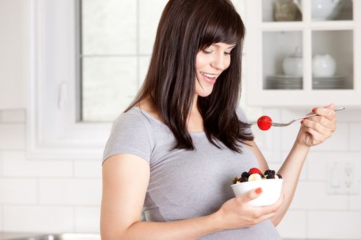 Happy pregnant woman eating healthy bowl of fresh fruit