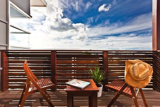 Stylish wooden furniture on an outdoor deck with a wooden railing consisting of two chairs and a low table with a cowboy hat slung over one of them