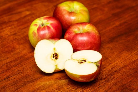 Three red and green apples on a wood table with one cut in half