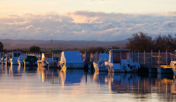 Small fishing and pleasure boats moored in a tranquil marina at sunset reflected in the glow of the sun