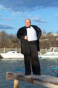 Overweight man in tuxedo standing on the pier marina