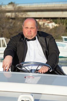Overweight man in a tuxedo at the helm of a pleasure boat, closeup