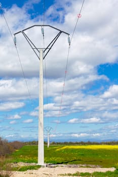 Row of rural electrical power lines crossing an empty open green field
