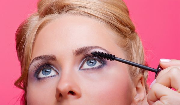 Beautiful woman applying mascara on her eyelashes