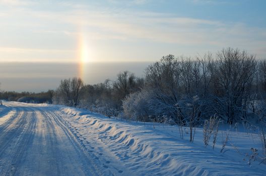 Road in a countryside in sunny winter rainbow day.Frozen trees in snowy field