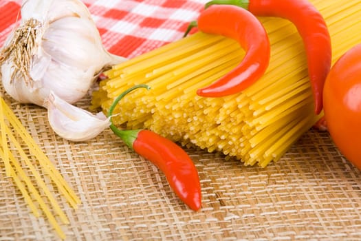 Golden raw dried Italian pasta with other ingredients on kitchen desk.