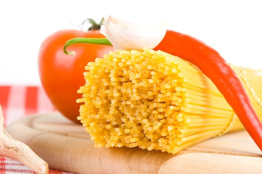 Golden raw dried Italian pasta with other ingredients on kitchen desk.