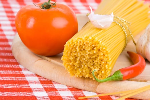 Golden raw dried Italian pasta with other ingredients on kitchen desk.