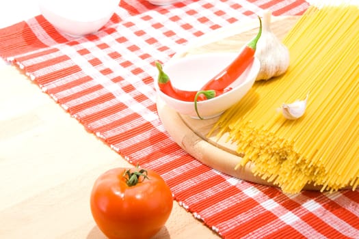 Golden raw dried Italian pasta with other ingredients on kitchen desk.