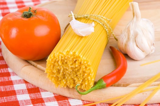 Golden raw dried Italian pasta with other ingredients on kitchen desk.