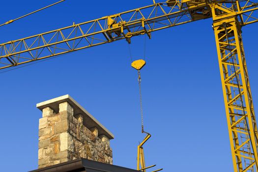 Yellow crane and blue sky on building site with roof and chimney