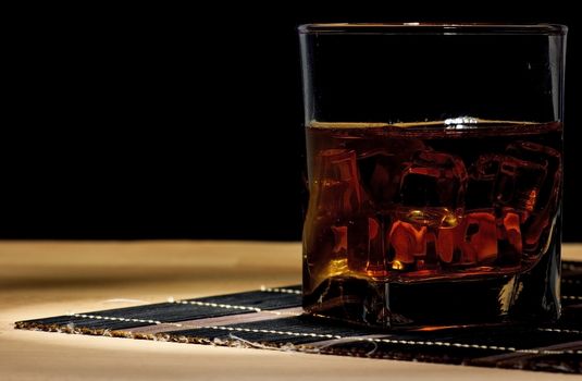A glass of aged old whiskey on the rocks on black background