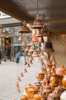 clay pots and hanging bells wares sold in outside store shop market and people walk in city street.