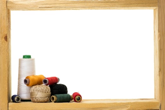 Spools with colored sewing thread inside rough wooden frame on white background 
