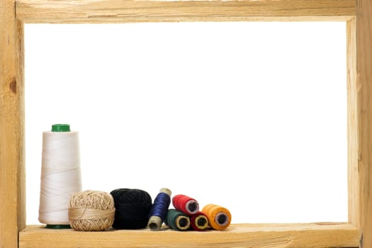 Spools with colored sewing thread inside rough wooden frame on white background 