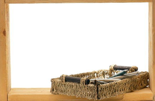 Wicker basket with a ball-point pens and brushes in a wooden frame on white background